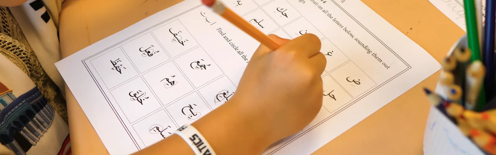 A Juniors student tracing Arabic letters on a Qāʿidah worksheet